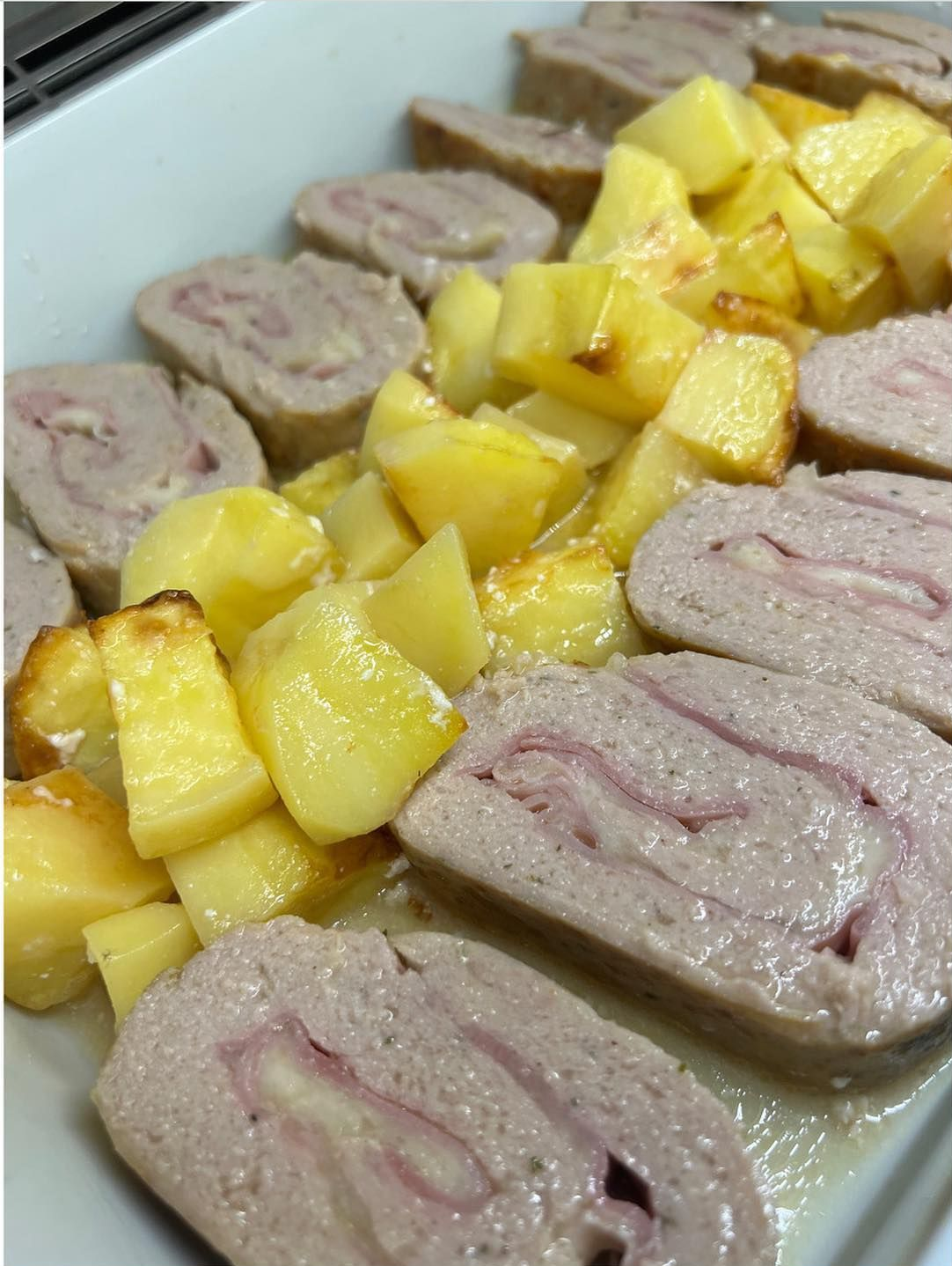 Rotolo di carne affettata con prosciutto al centro, servito con patate arrosto dorate.