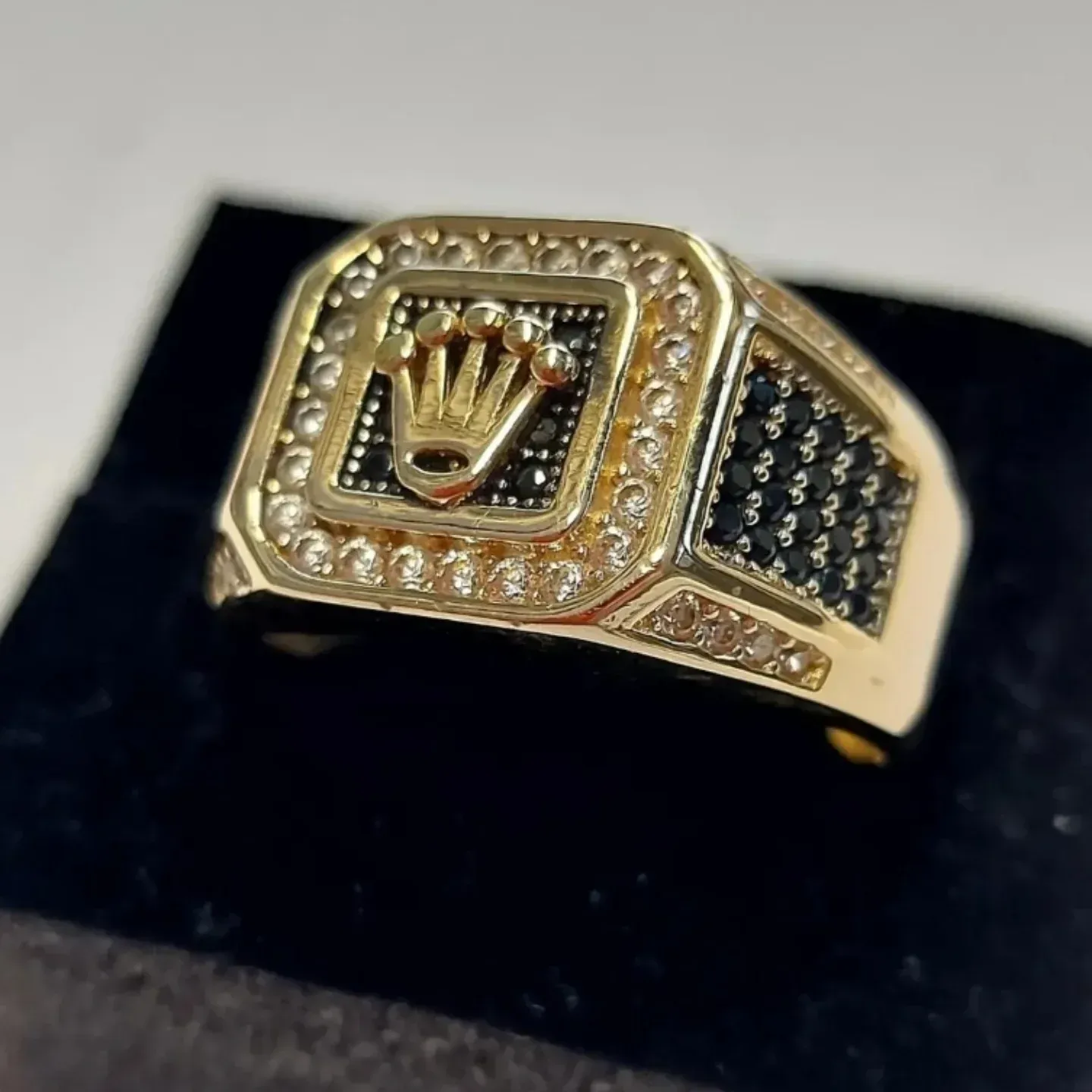 Anello in oro e pietre preziose nere con emblema a corona su piedistallo scuro.
