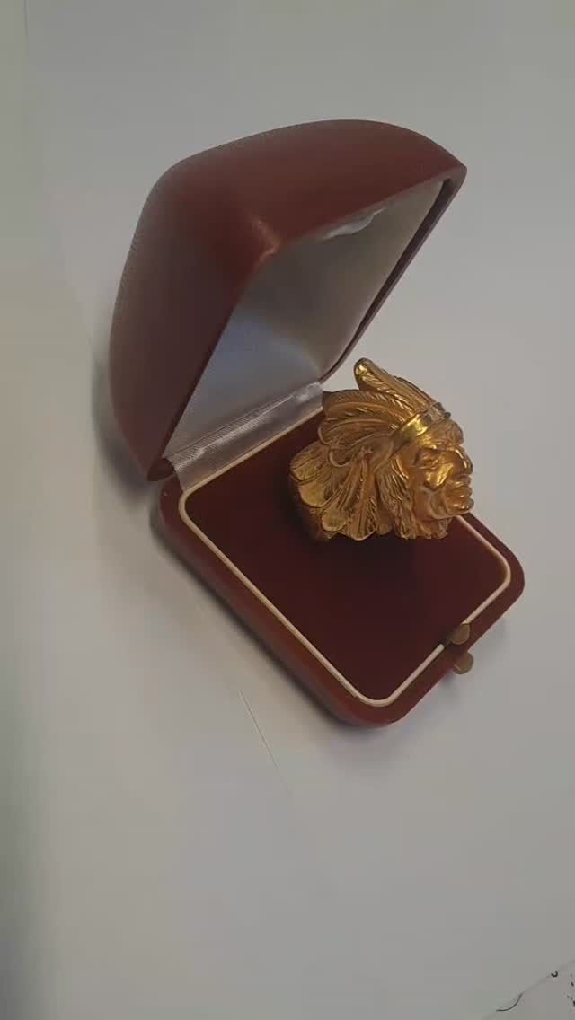 Scatola portagioie in velluto rosso aperta, contenente un anello dorato a forma di fiore su una superficie bianca.