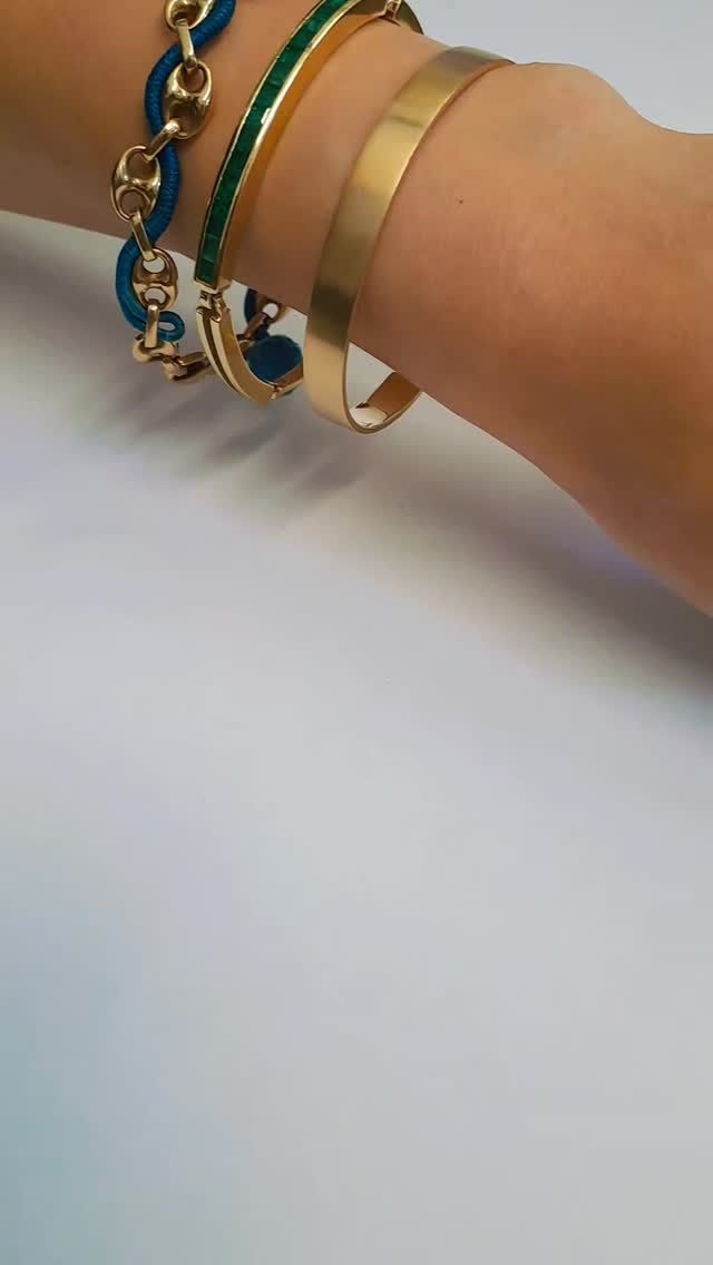Primo piano di un polso con braccialetti dorati e blu su sfondo bianco.