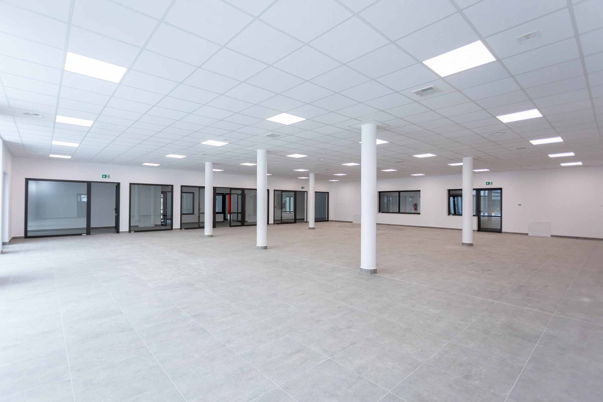 Empty bright office space with white ceiling, pillars, and glass-walled rooms