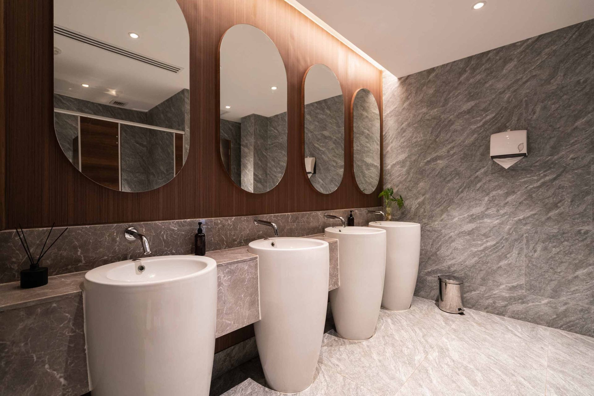 Modern bathroom with marble walls, round mirrors, and white pedestal sinks