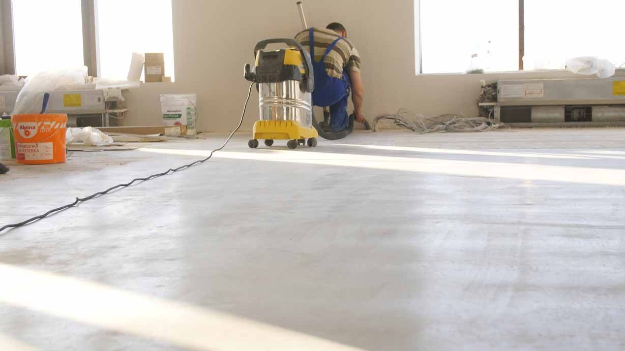 Worker using a yellow floor sander in a bright room under construction