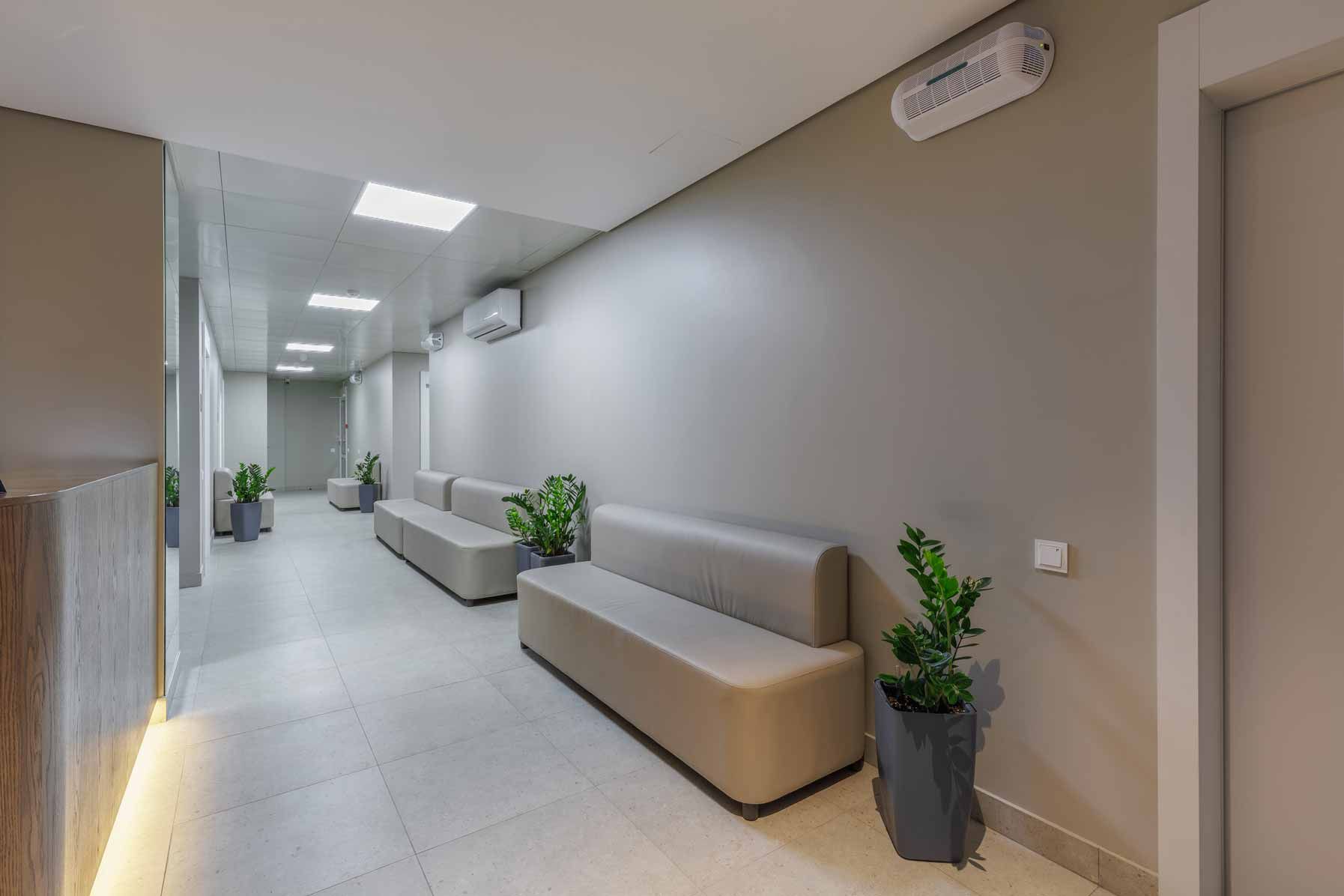 Modern hallway with gray walls, long benches, potted plants, and bright ceiling lights