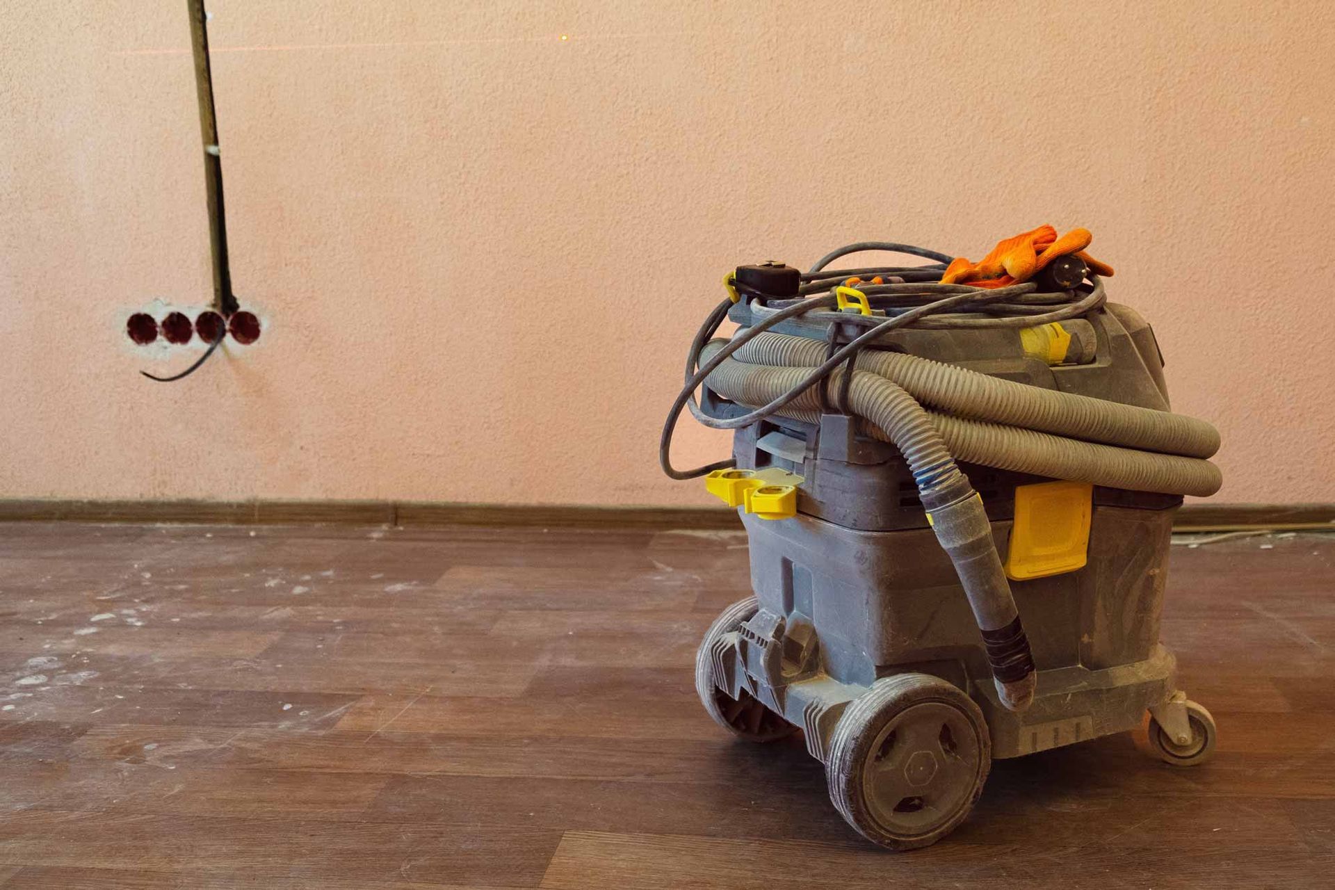 Floor sander on a dusty wooden floor with coiled hoses and tools in an empty room