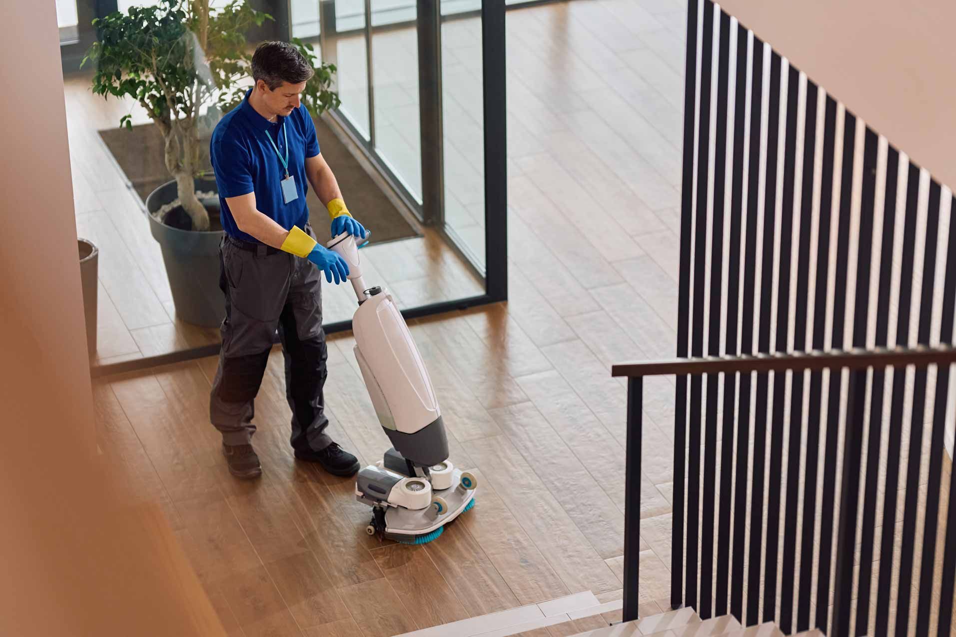 Person in blue uniforms a floor with a white floor-cleaning machine in a modern indoor space