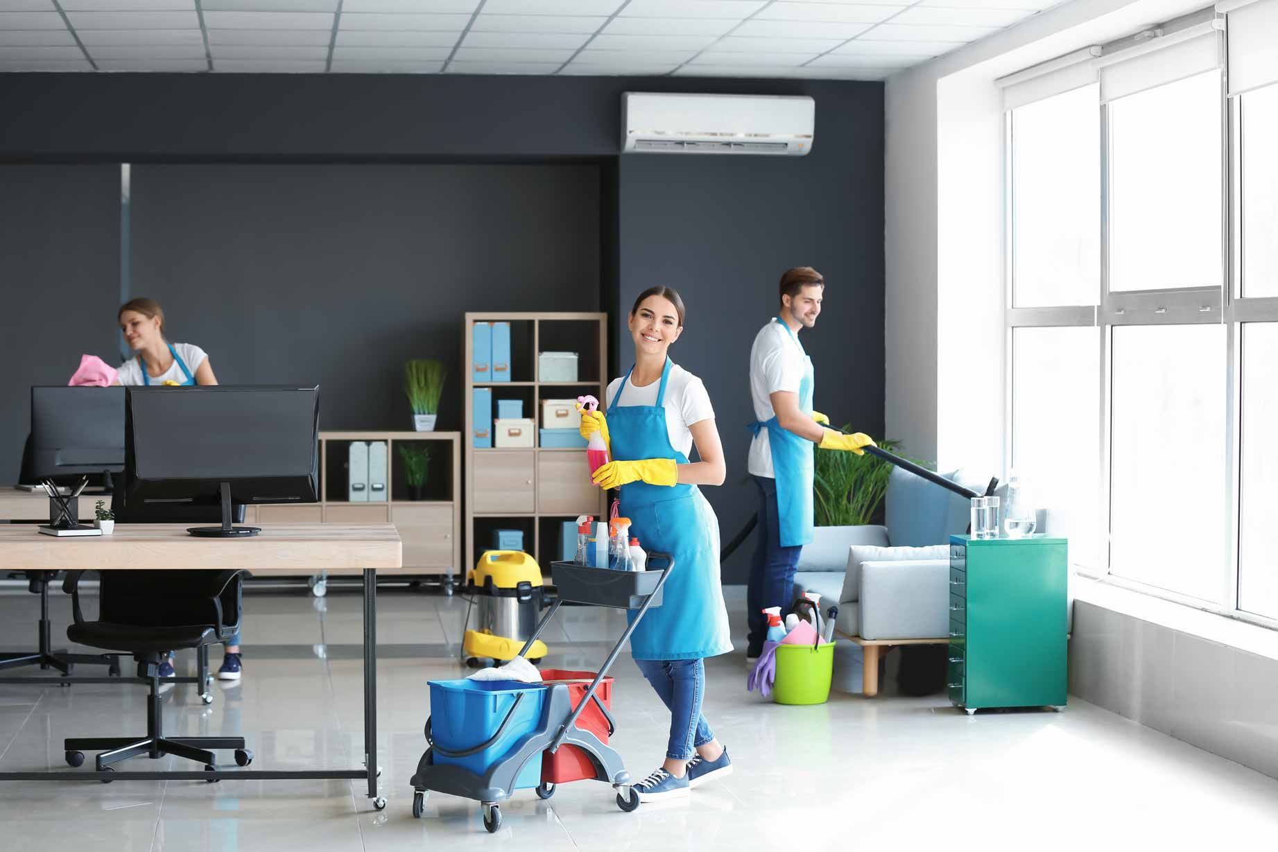 Office staff cleaning a modern workspace with mops, buckets, and supplies near desks and windows