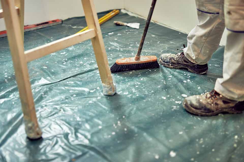 Worker sweeping water from a floor covered with a green tarp during cleanup