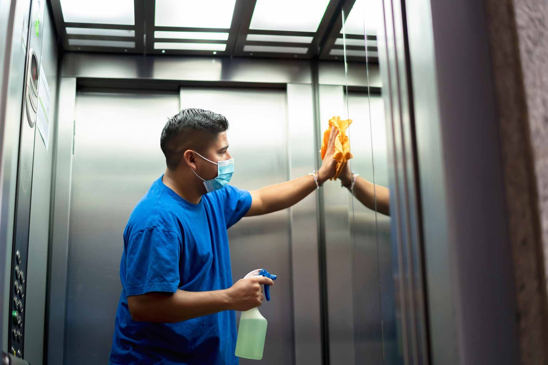 Person in blue shirt cleaning an elevator mirror with a spray bottle and cloth.