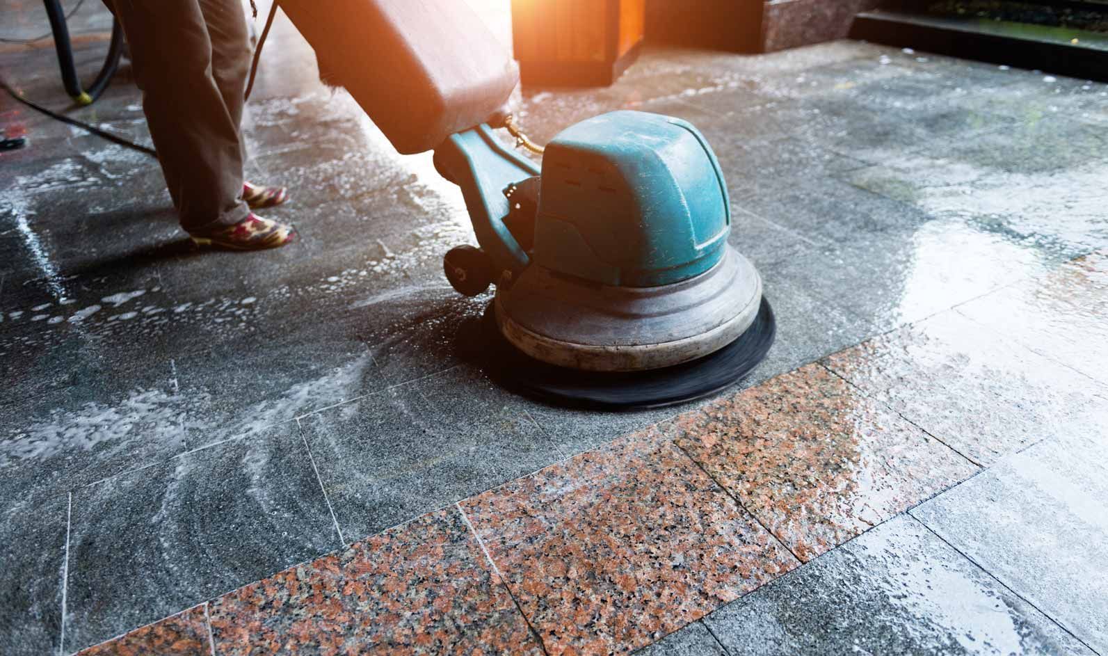 Person uses a blue floor buffer to polish a wet stone floor indoors