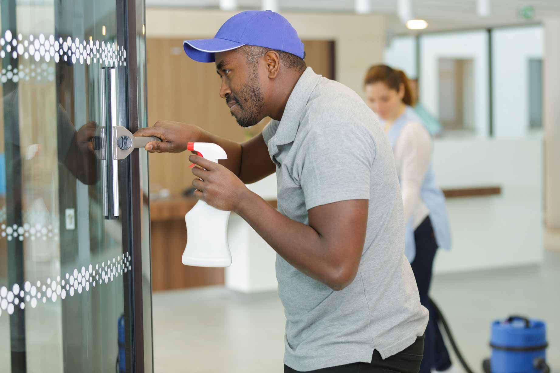 Man cleaning a glass door with a spray bottle and cloth in a hallway