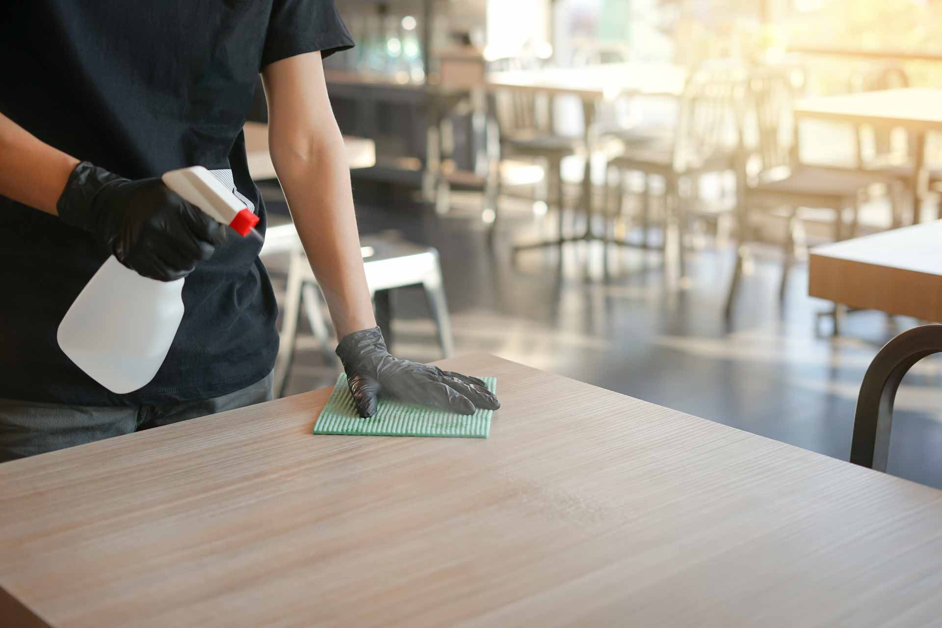 Person spraying and wiping a wooden table in a bright café