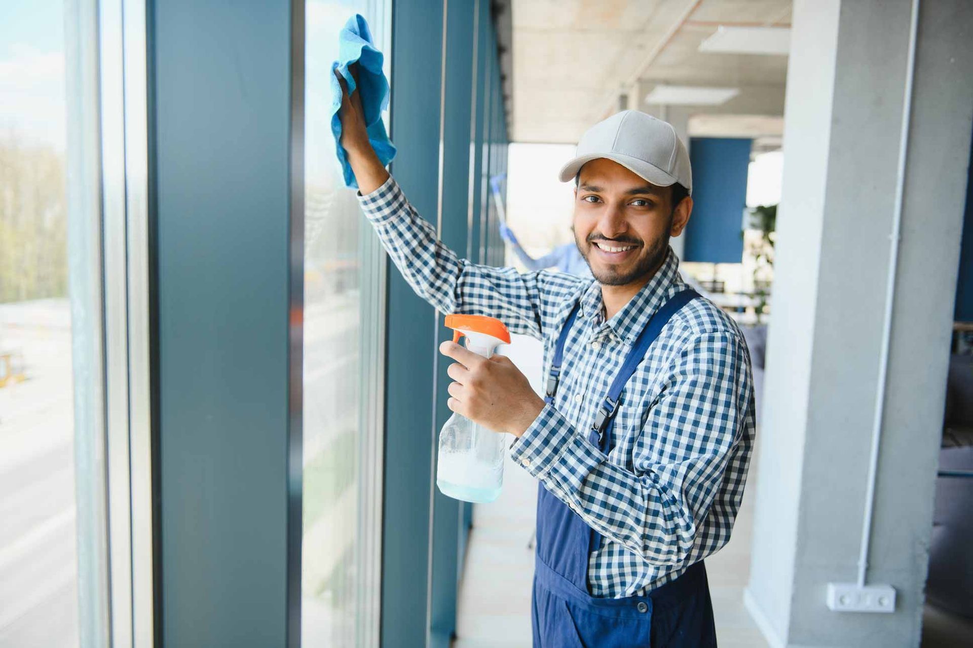 Cleaner wiping a glass wall with spray bottle in a bright office hallway