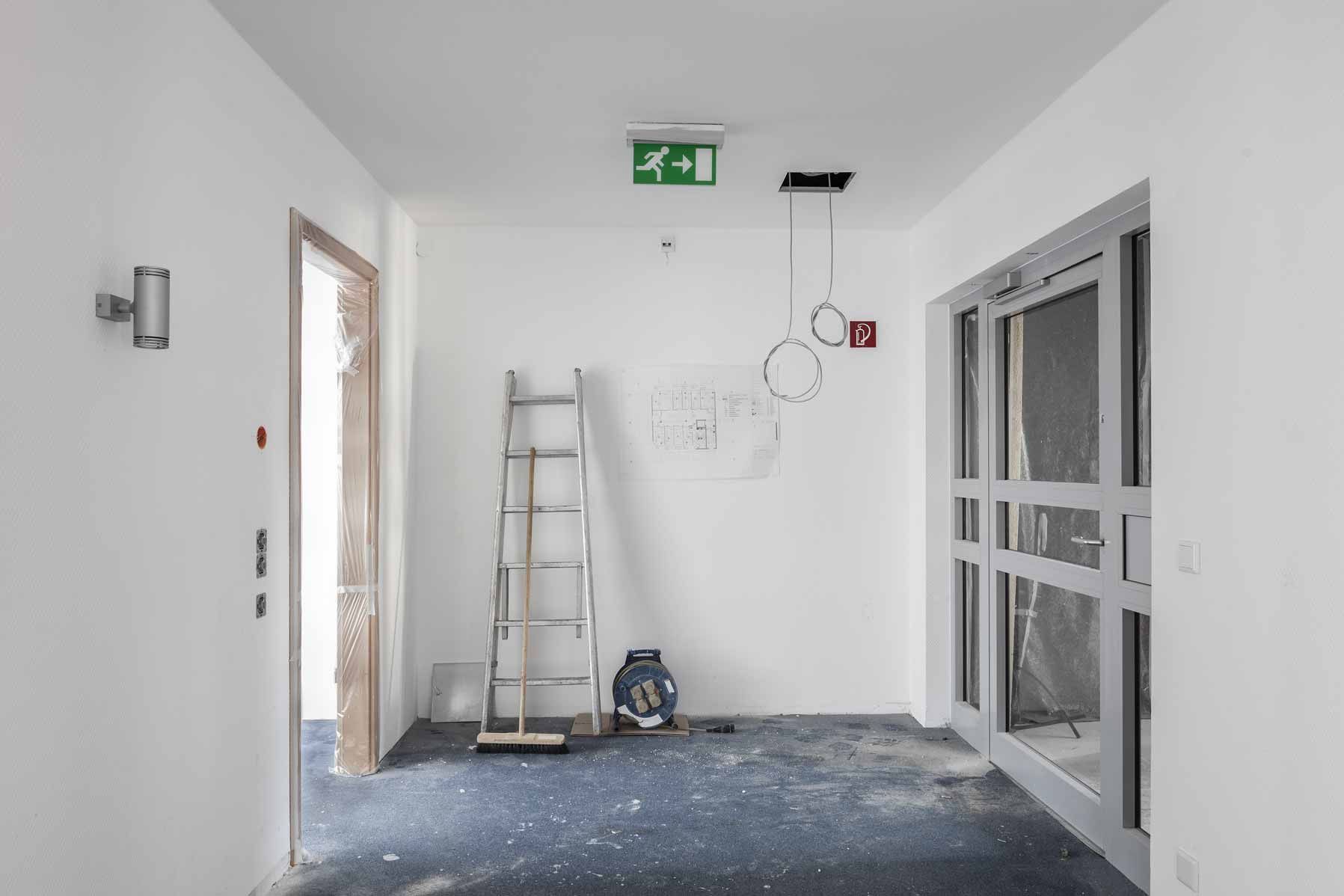Empty white hallway under renovation with a ladder, tools, debris, and glass doors.