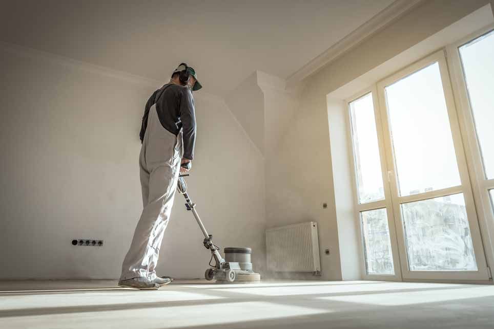 Person using a floor buffer in a bright, empty room near large windows.