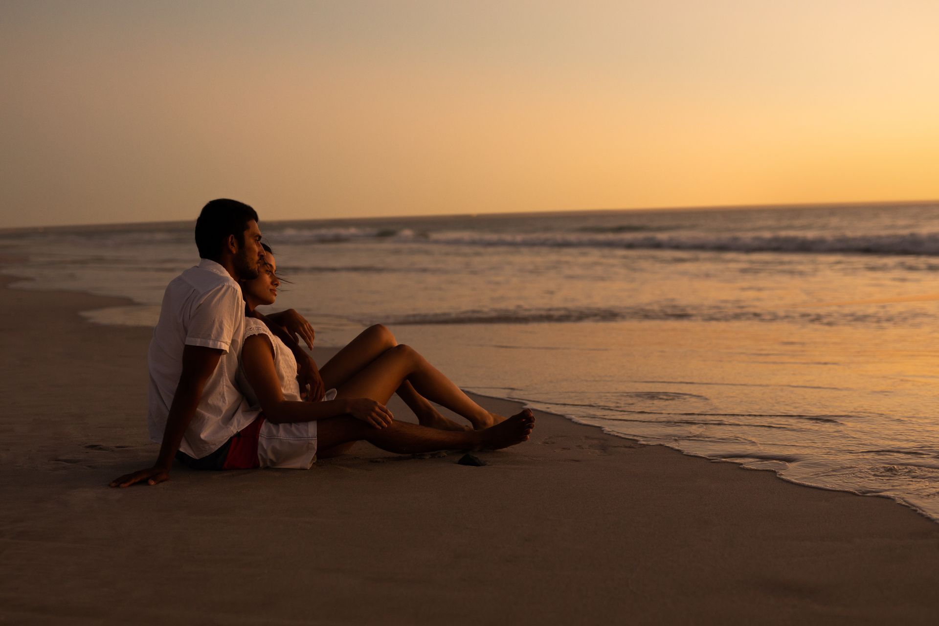 Casal sentado na areia da praia vendo o pôr do sol em Balneário Camboriú