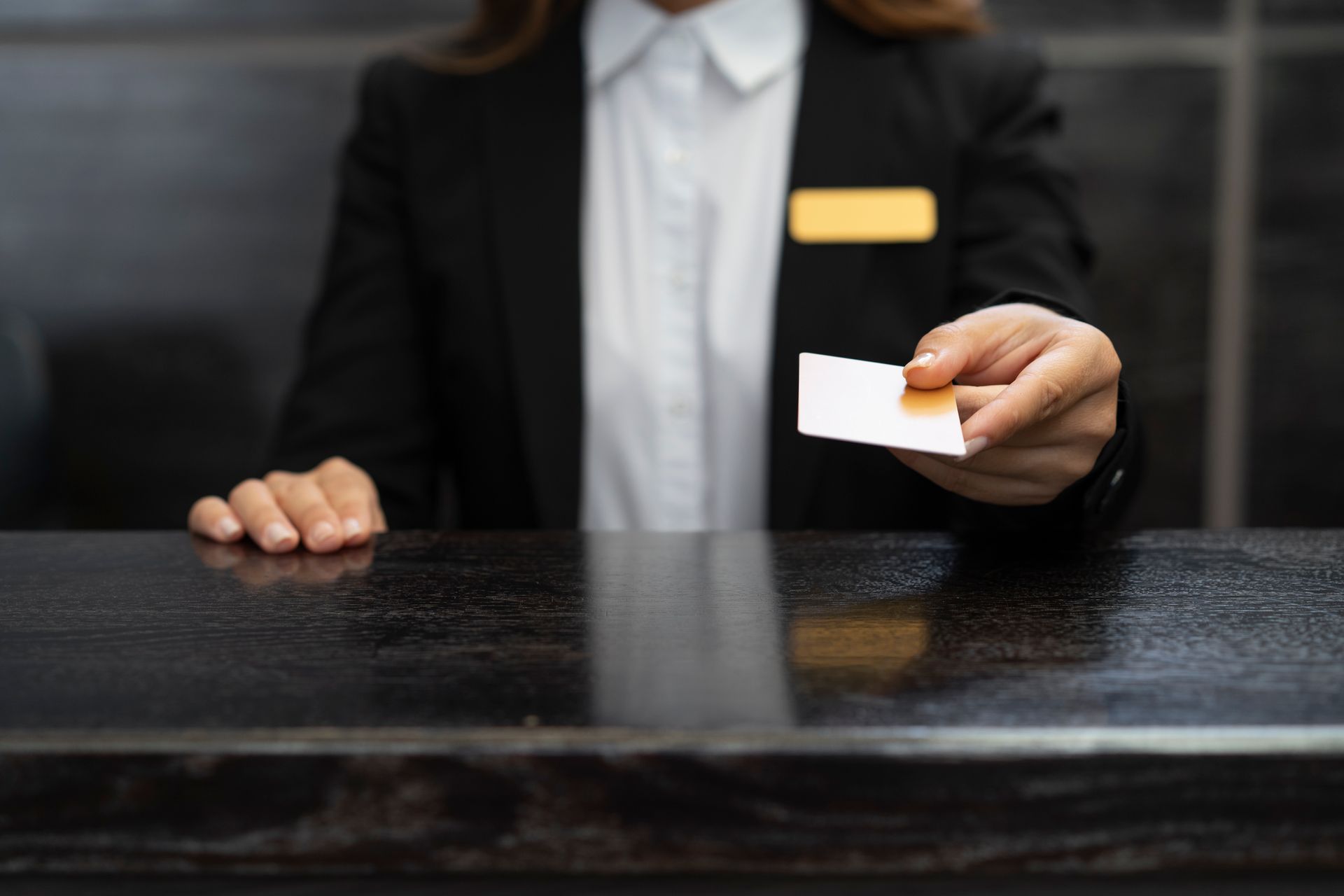 Recepcionista de hotel entregando cartão de acesso sobre balcão escuro.