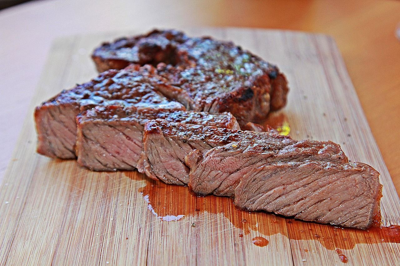 Corte de carne grelhada, fatiada sobre tábua de madeira, com suculência e textura no ponto médio.