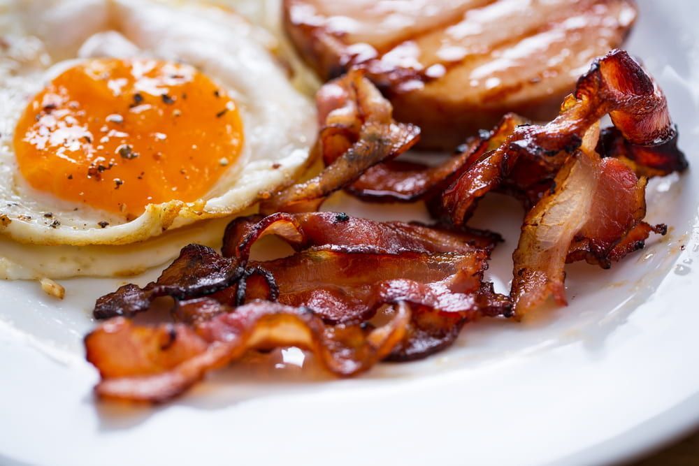 A White Plate Topped with Eggs , Bacon and Ham — Brews & Bites Beachside Cafe in Meikleville Hill, QLD