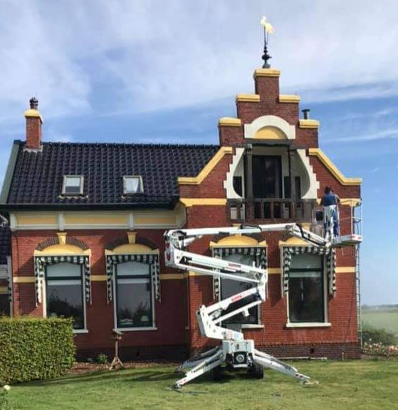 A man is standing on a lift in front of a brick house