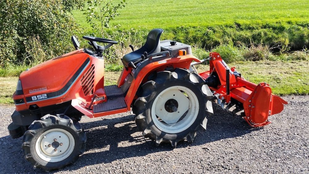 An orange tractor is parked on the side of the road next to a field.