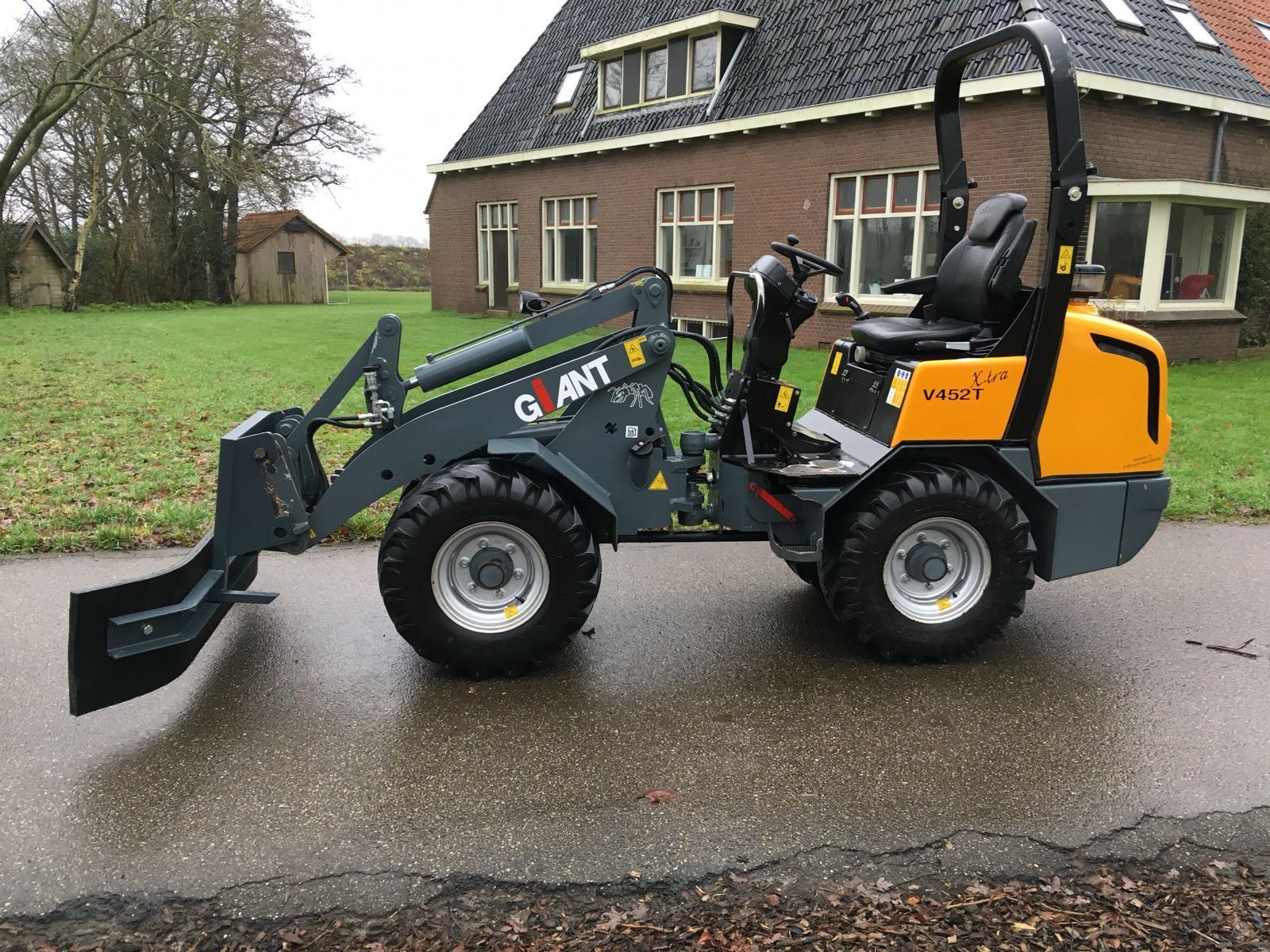 A small tractor is parked on the side of the road in front of a house.
