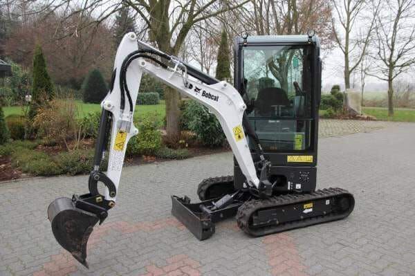 A small excavator is parked on a brick driveway.
