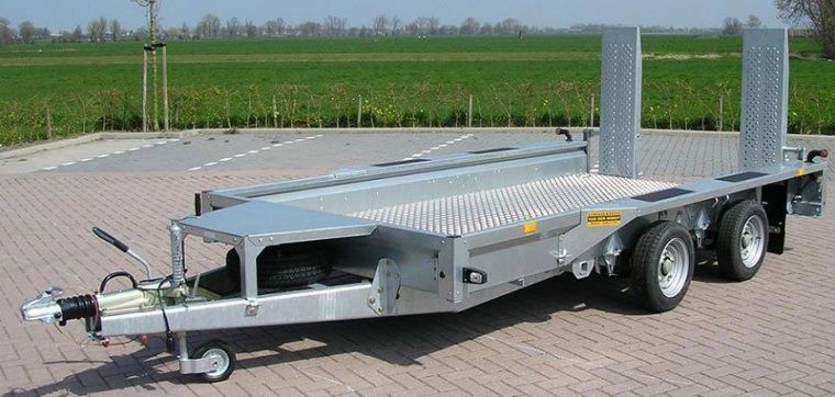 A trailer is parked on a brick pavement in front of a field.