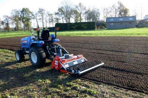 A tractor is plowing a field with a machine attached to it.