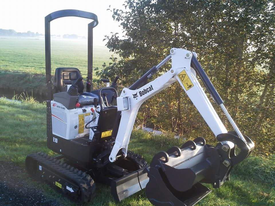 A small bobcat excavator is parked in a grassy field