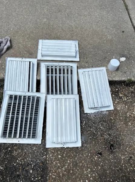 Several white vent grilles and covers arranged on concrete beside a curb, with a small cup nearby