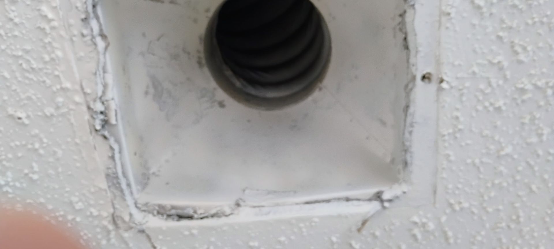 Close-up of a white wall vent opening with a dark circular pipe inside