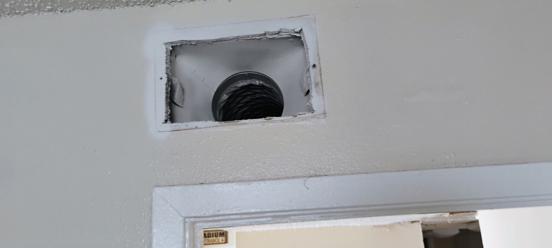 Vent opening in a ceiling above a doorway, with white trim and unfinished edges