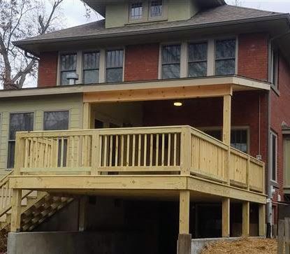 A large brick house with a wooden deck and stairs.