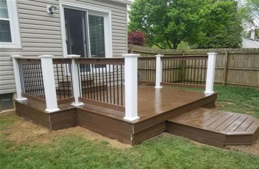 A wooden deck with white railings is in the backyard of a house.