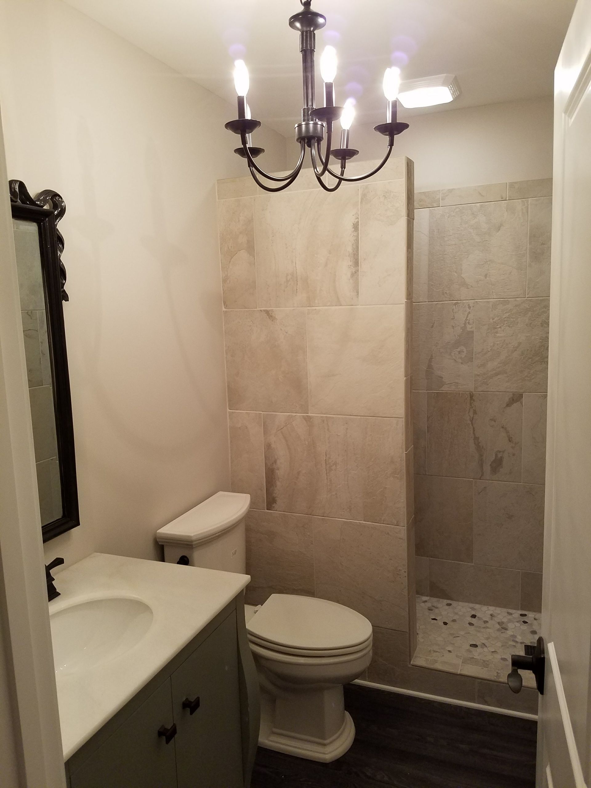 A bathroom with a toilet , sink , mirror and chandelier.