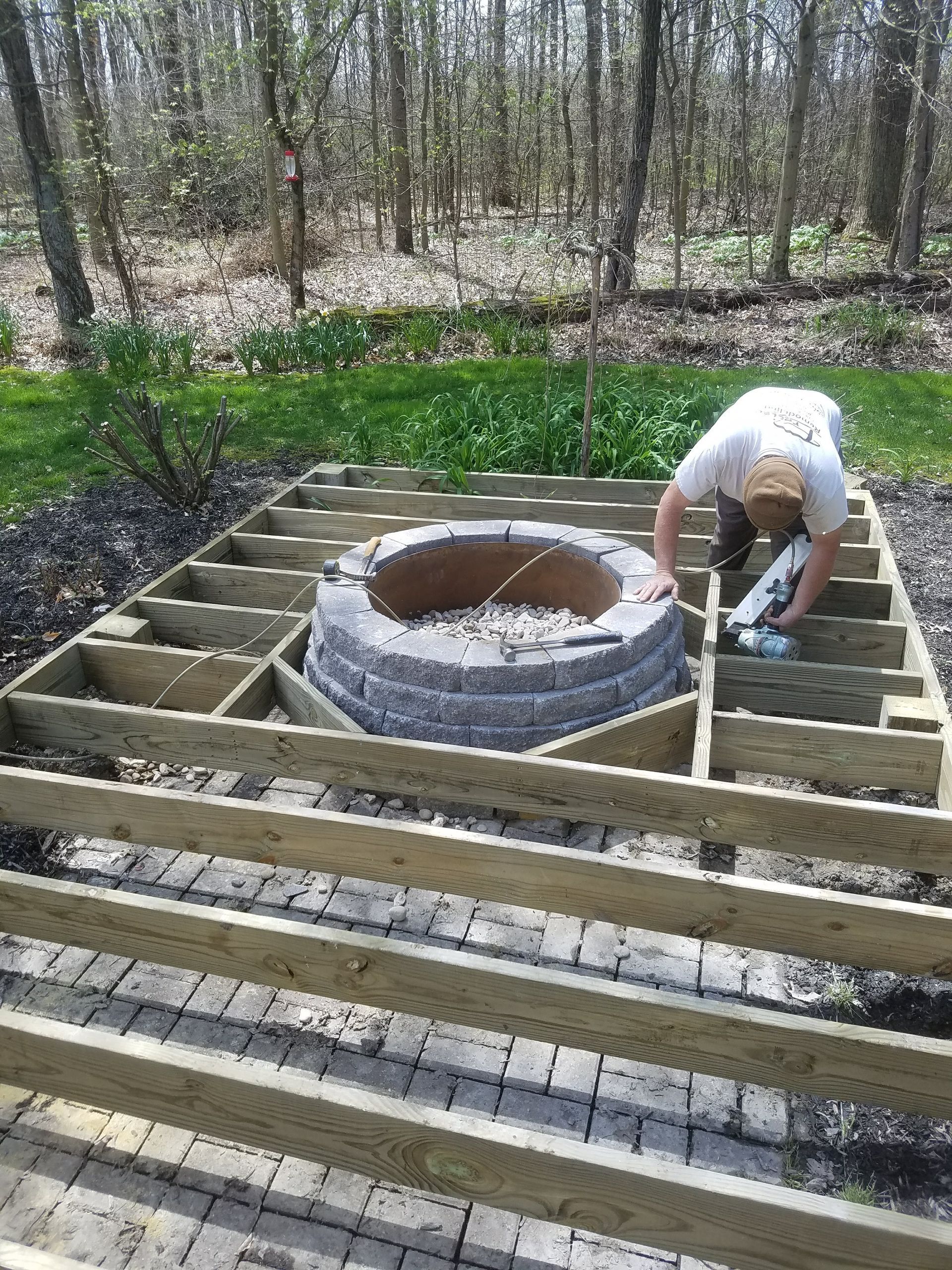 A man is working on a wooden deck around a fire pit.