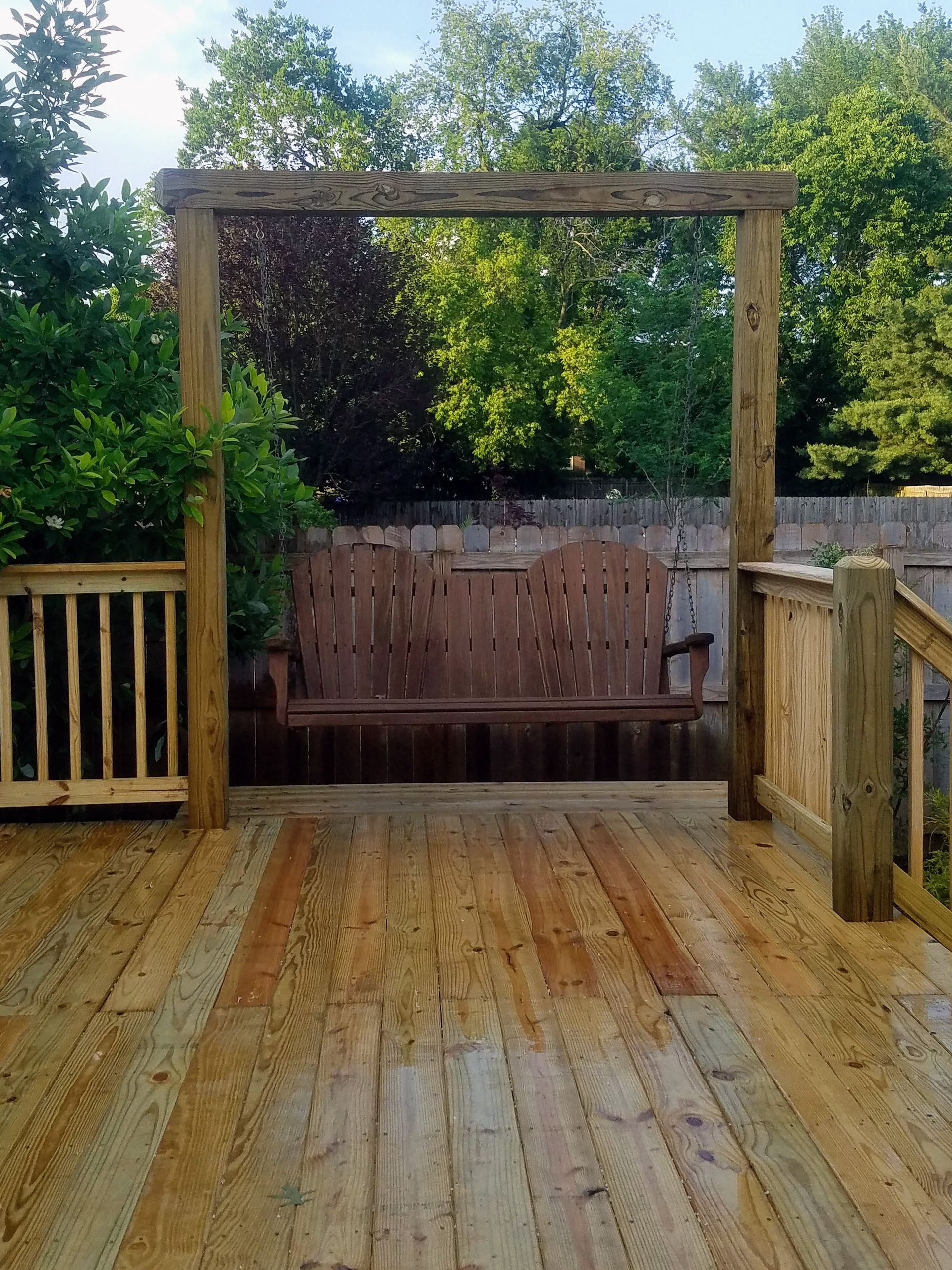 A wooden deck with a swing in the middle of it.