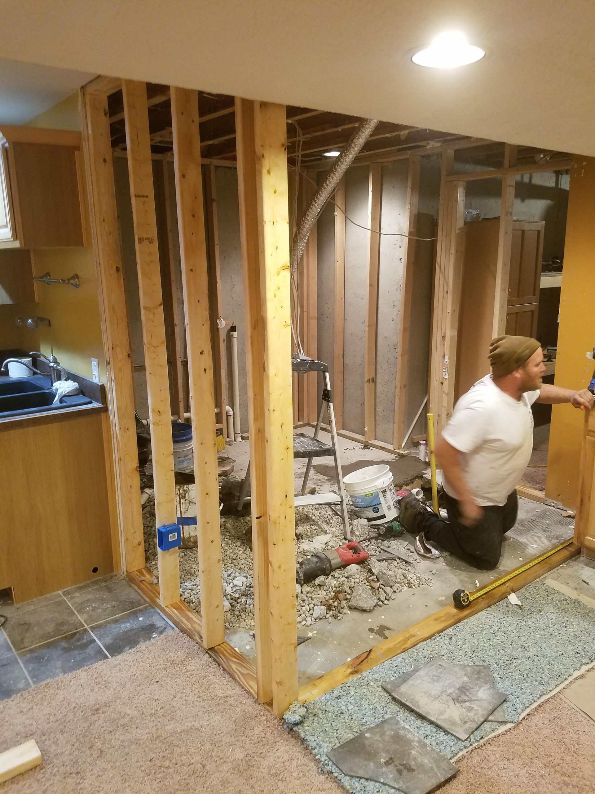 A man is kneeling on the floor in a room under construction.