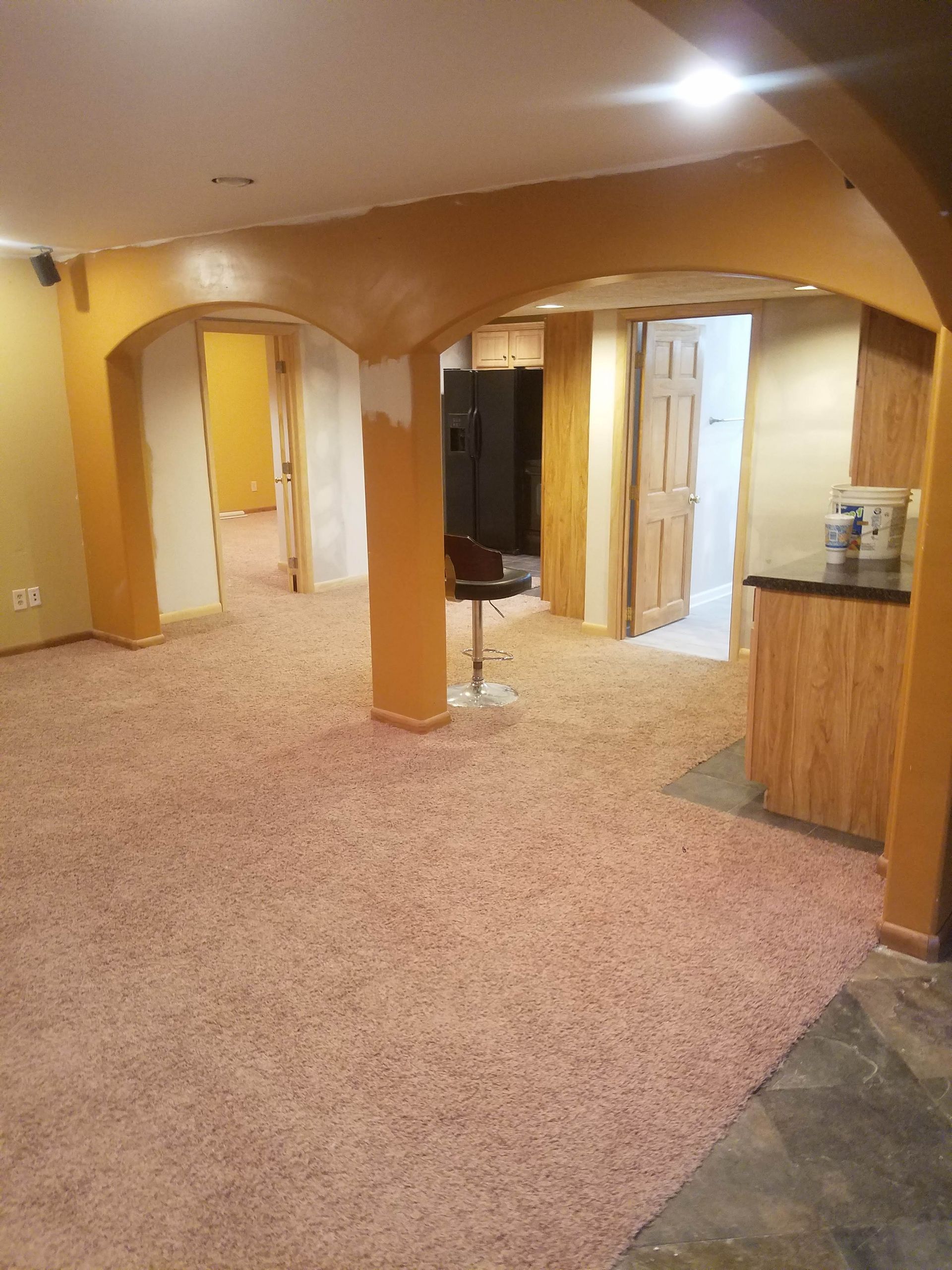 A basement with a carpeted floor and a bar stool.