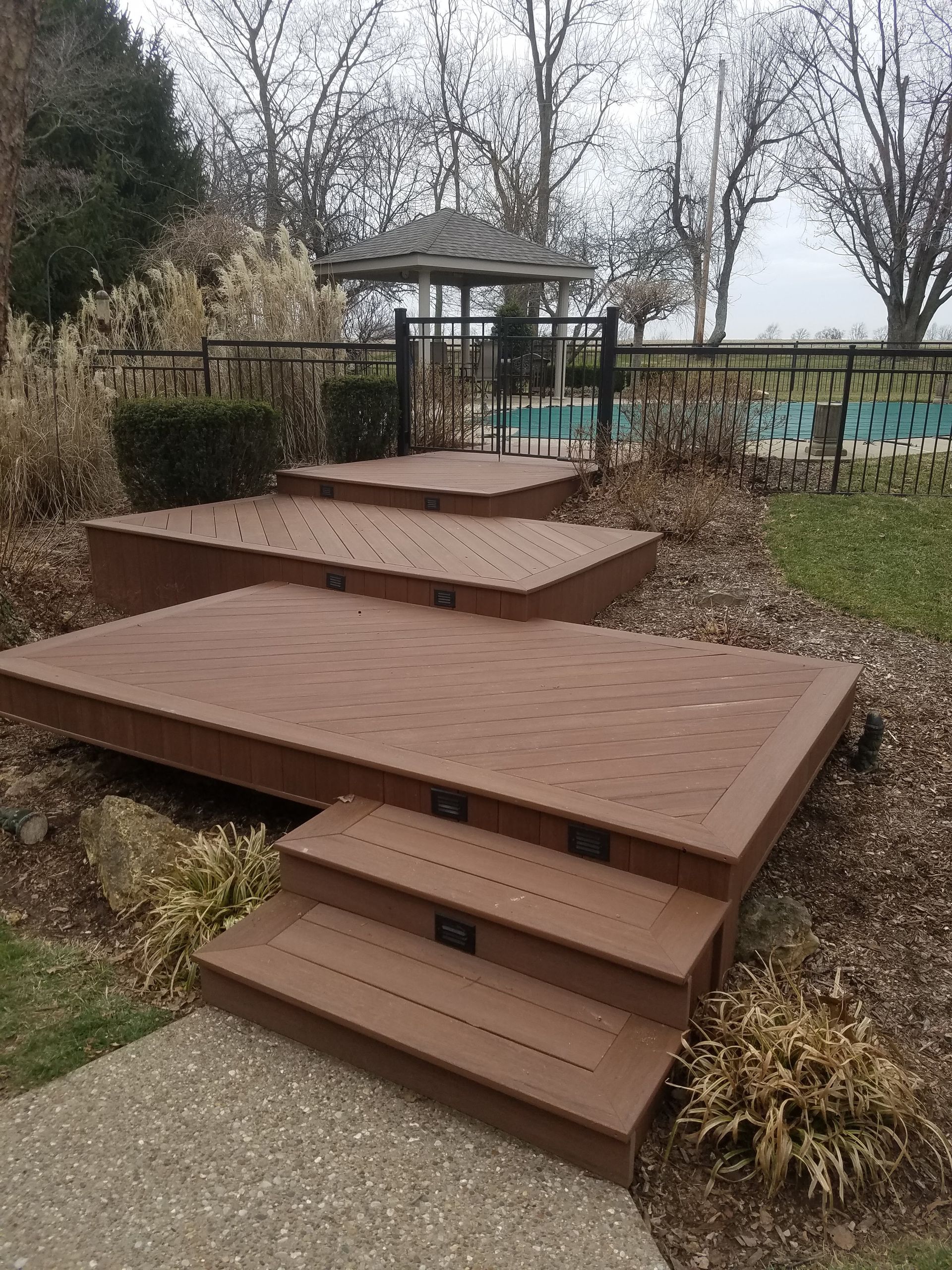 A wooden deck with stairs leading up to it and a gazebo in the background.