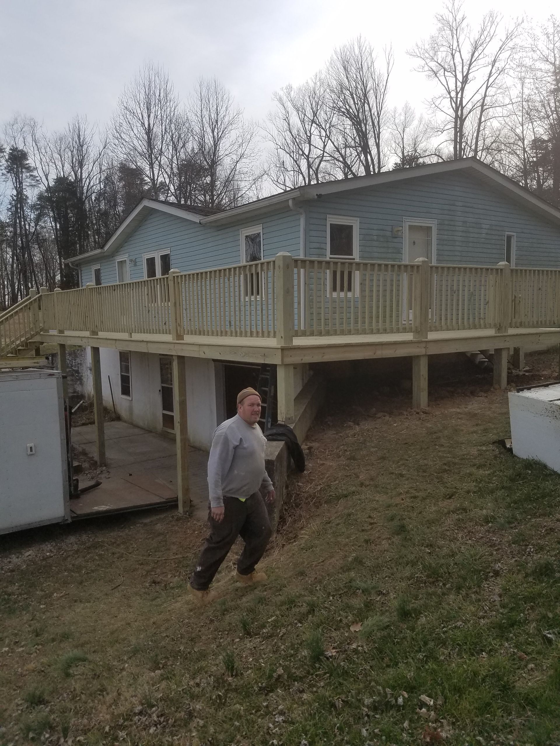 A man is standing in front of a house with a wooden deck.