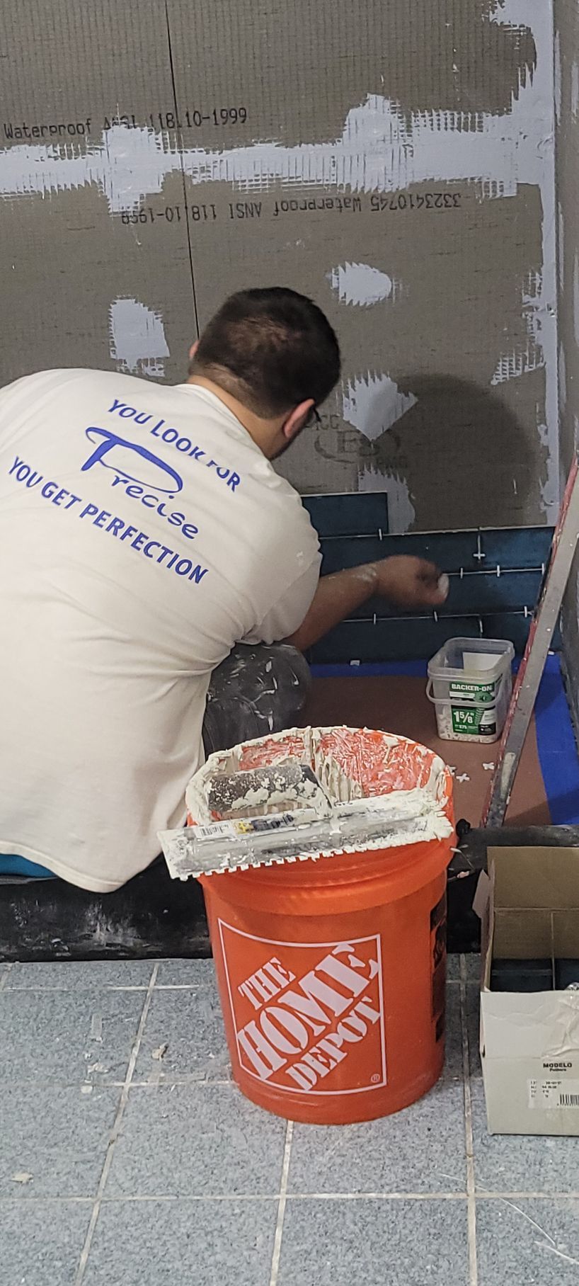 A man is working on a wall next to an orange bucket.
