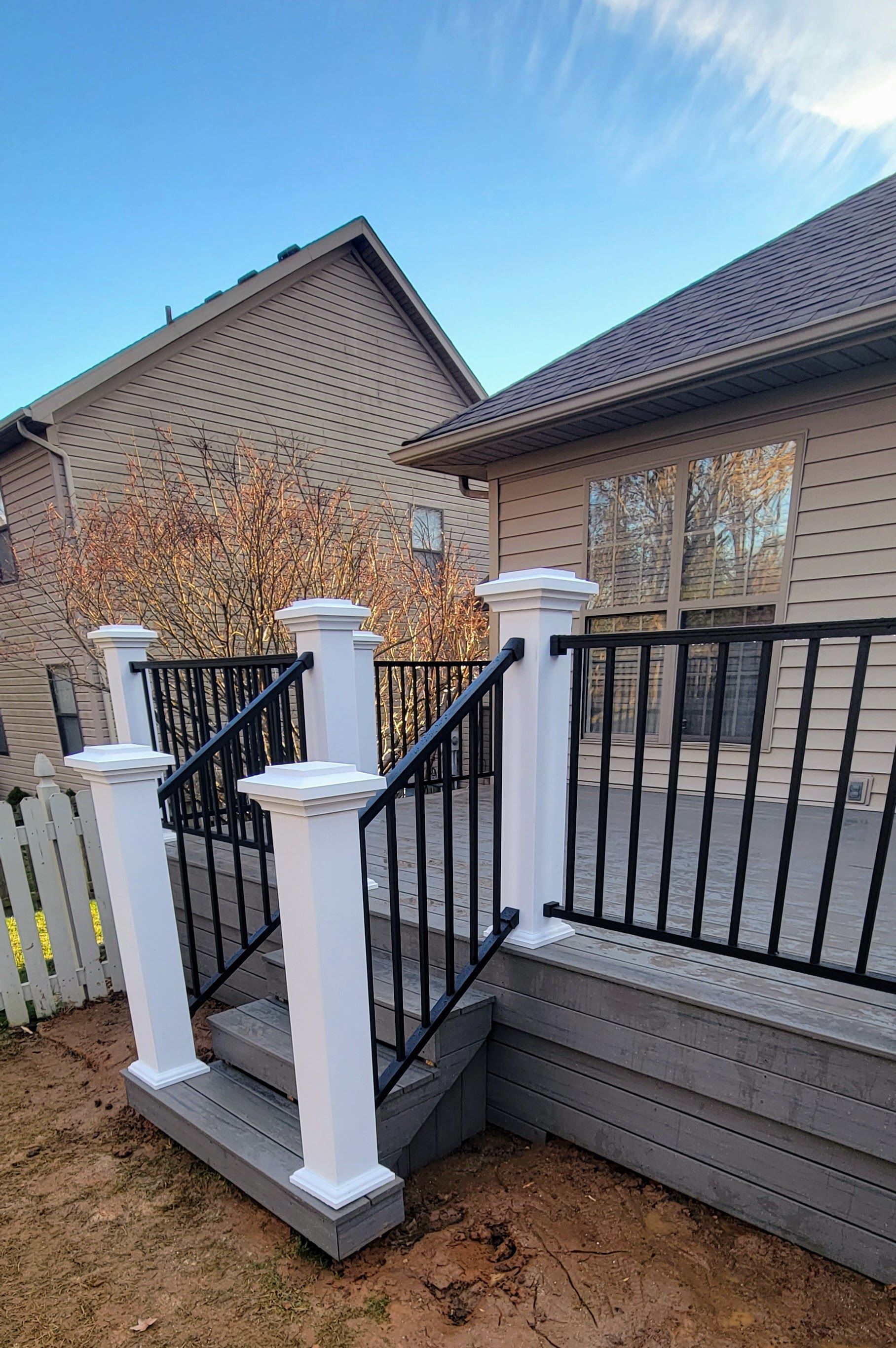 A deck with stairs and a black railing in front of a house.