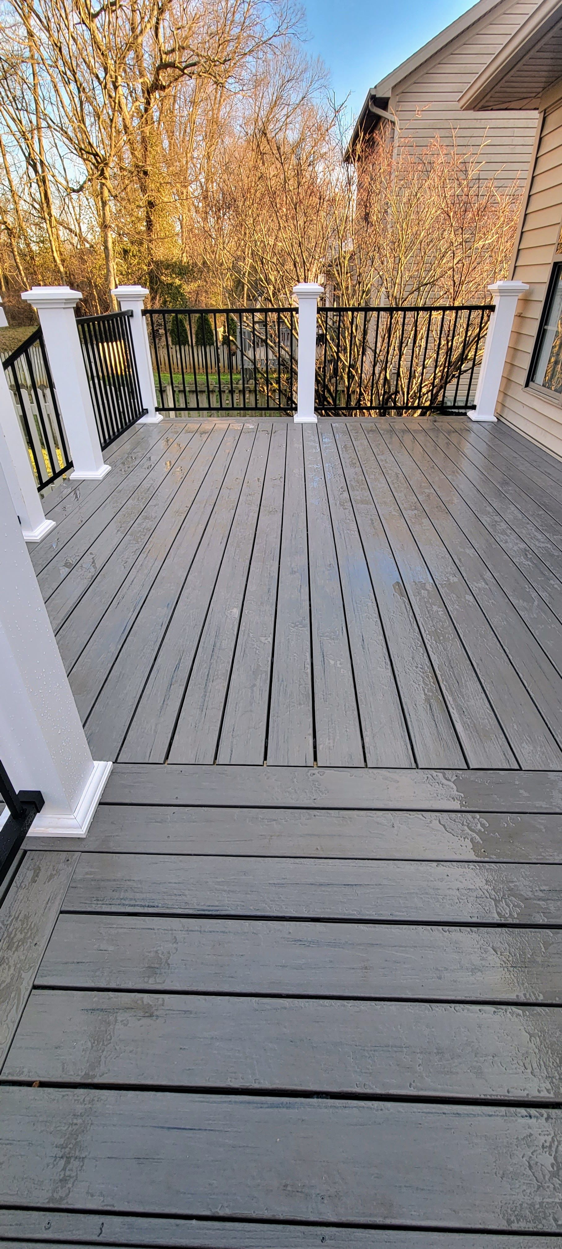 A large wooden deck with a metal railing and a house in the background.