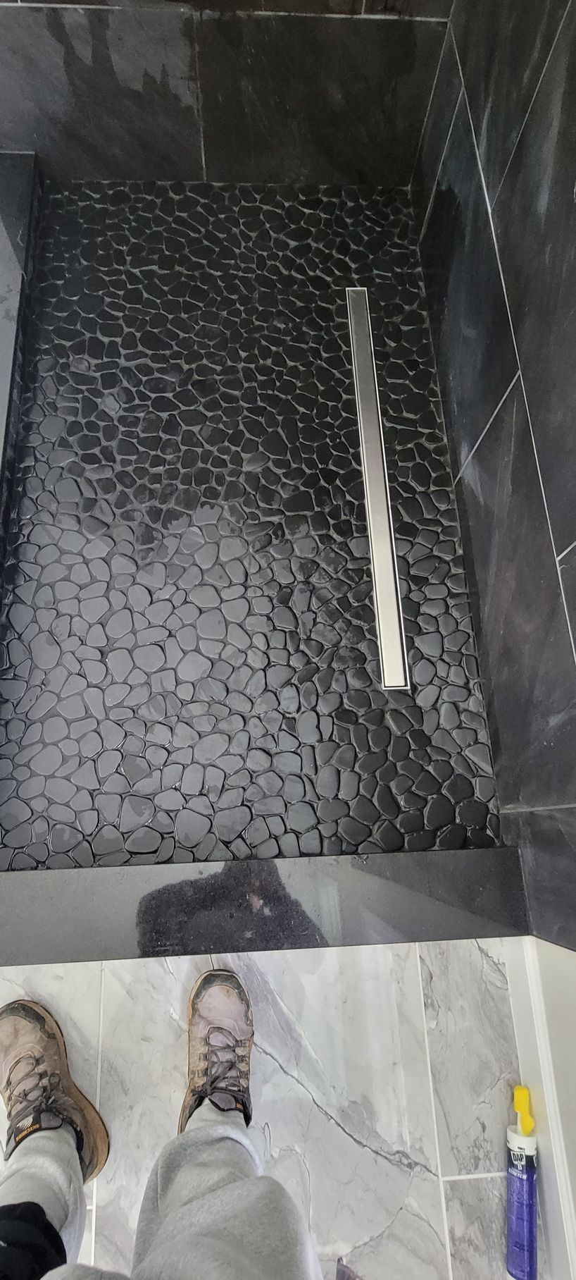 A person is standing in a shower with a black tile floor.