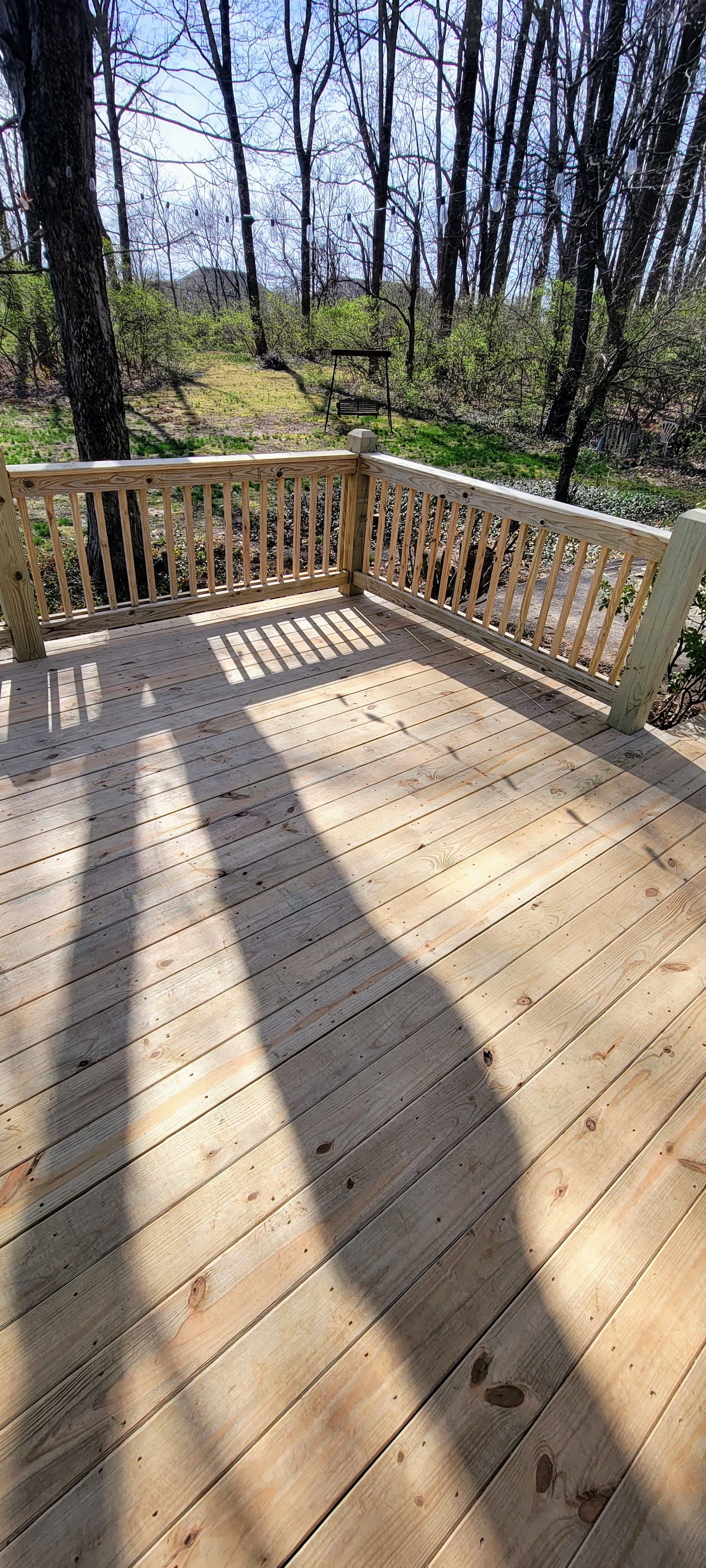 A wooden deck with a railing and trees in the background.