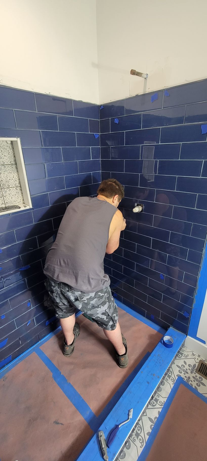 A man is kneeling down in a bathroom with blue tiles.