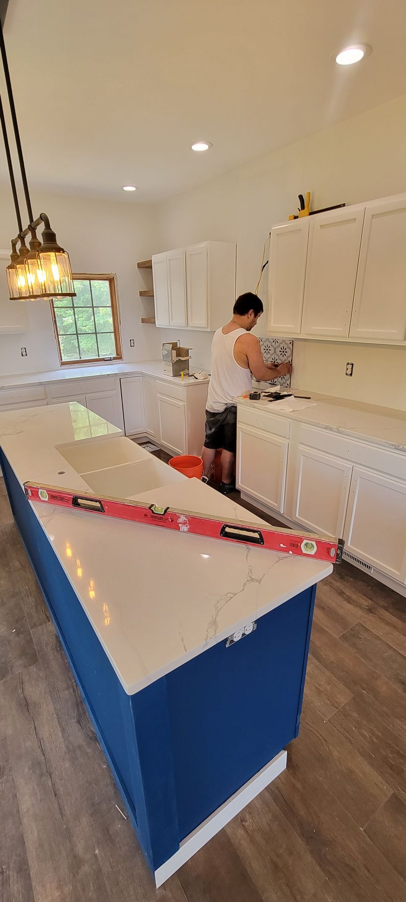 A man is working on a kitchen with white cabinets and a blue island.