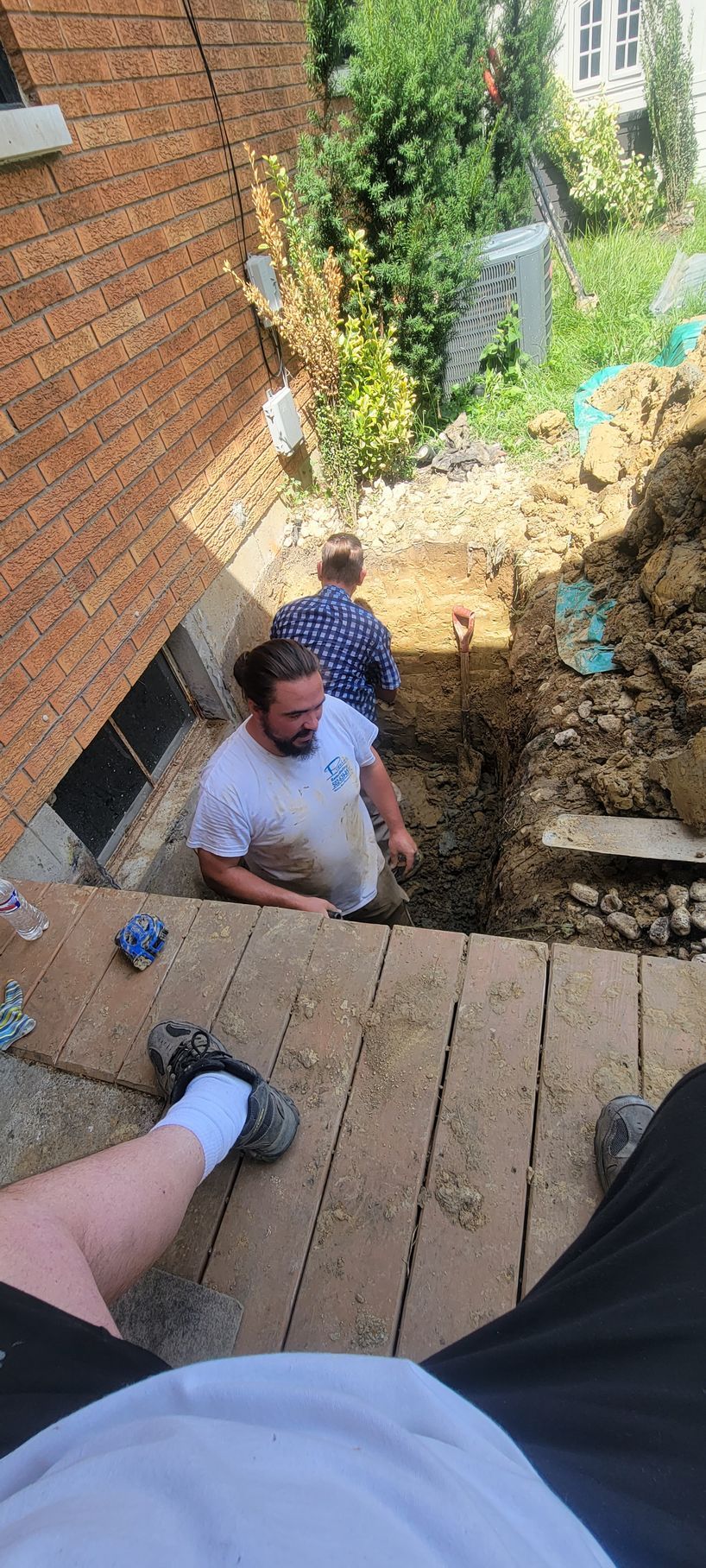 A group of men are digging a hole in the ground in front of a brick building.